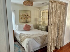 Une chambre à coucher avec un lit, une table de chevet, une lampe, un rideau en macramé et un tableau au mur.