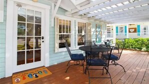 Eine überdachte Terrasse mit Tisch und Stühlen, eine Tür mit Fensterglas und eine Veranda mit Geländer.
