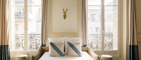 Hotelkamer met een groot bed, twee nachtkastjes, een decoratief wandobject en uitzicht op de stad door grote ramen.