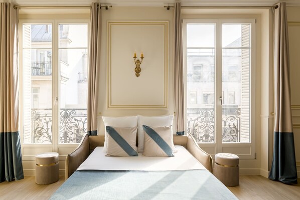 Ein Hotelzimmer mit einem großen Bett, zwei Nachttischen, einer Wanddekoration und Blick auf die Stadt durch große Fenster.
