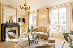 A spacious living room with a fireplace, a sofa, a coffee table, and a TV mounted on the wall. - Merveil - Signature Suite - Louvre - Opera I (Paris)