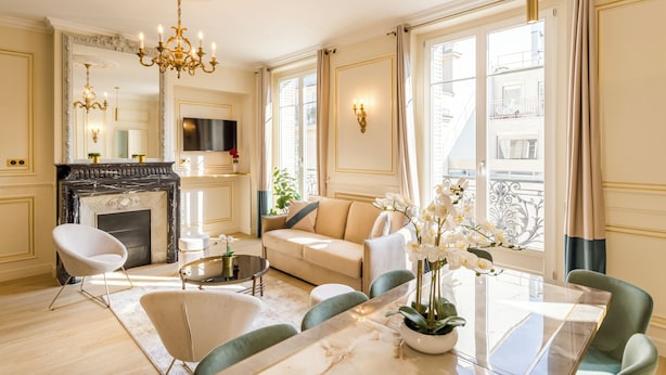 A luxurious living room with a fireplace, comfortable seating, and large windows. - Merveil - Signature Suite - Louvre - Opera I (Paris)