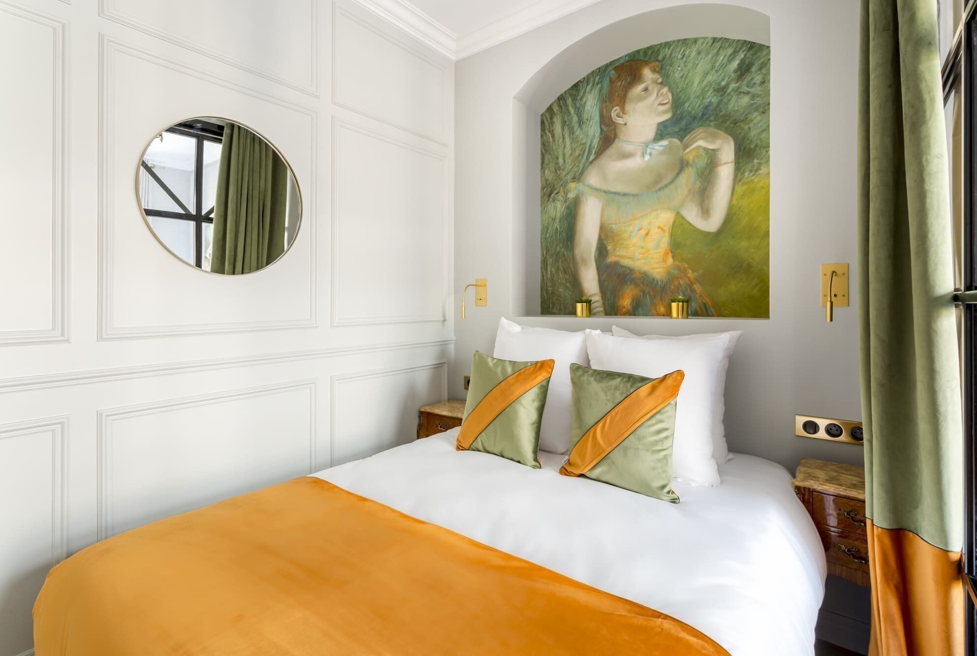 Une chambre d’hôtel avec un lit, un miroir rond, un tableau et une coiffeuse avec un miroir.