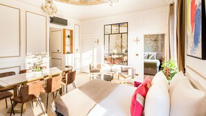 A well-lit hotel room with a large bed, a dining area, and a view of the city.