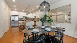 A modern kitchen with white cabinets, stainless steel appliances, and a dining area with a round table set for four. - Urban Oasis near Breweries & Old Town - Free Bikes (Fort Collins)