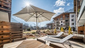 A wooden deck with lounge chairs and an umbrella, overlooking a mountainous landscape and buildings. - Le Gui- Lovely ground floor apartment in Chamonix (Chamonix)
