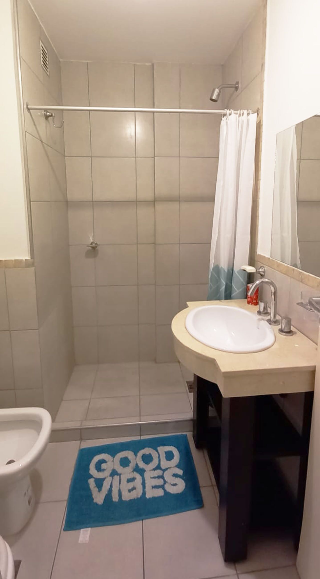 Een badkamer met een douche, een wastafel en een toilet. Er ligt een blauwe mat met de tekst 