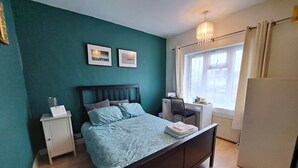 Ein Schlafzimmer mit Bett, Schreibtisch, Stuhl, Heizkörper und Fenster.