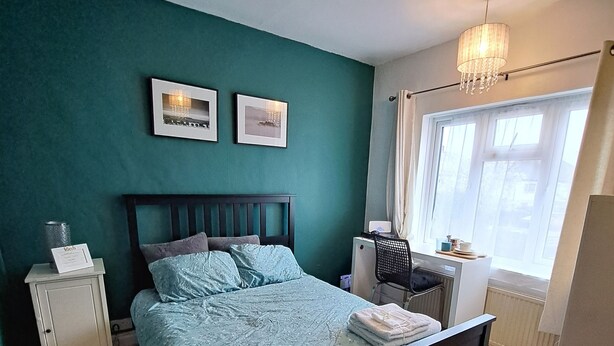 Ein Schlafzimmer mit Bett, Nachttisch, Heizkörper und einem Fenster mit Vorhängen.