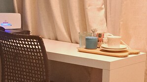 Ein kleiner, moderner Raum mit einem weißen Schreibtisch, einem schwarzen Mesh-Stuhl und einem kleinen Tisch mit Tasse und Untertasse.