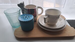 Ein Holztablett mit einem Glas, einer blauen Tasse, einer verzierten Tasse und einer weißen Tasse auf einem Tisch in der Nähe eines Fensters.