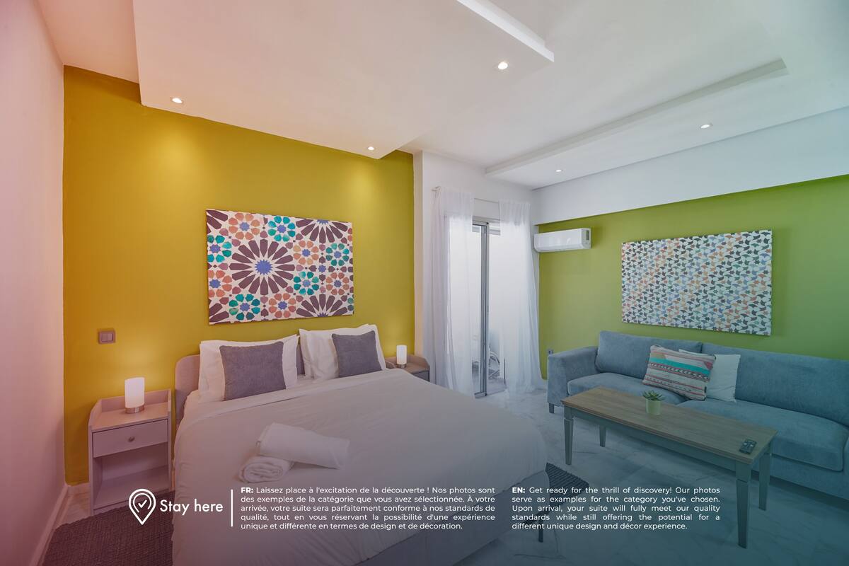 Quarto de hotel moderno com cama, sofá, mesa de centro e duas obras de arte na parede.