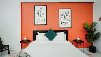 Un dormitorio moderno con una cama grande, una pared de acento naranja, dos cuadros enmarcados, un cojín verde y una planta en maceta.
