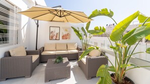 A sunlit outdoor seating area with wicker furniture, a large umbrella, and potted plants. - StayHere Rabat - Agdal Quiet Living (Rabat)