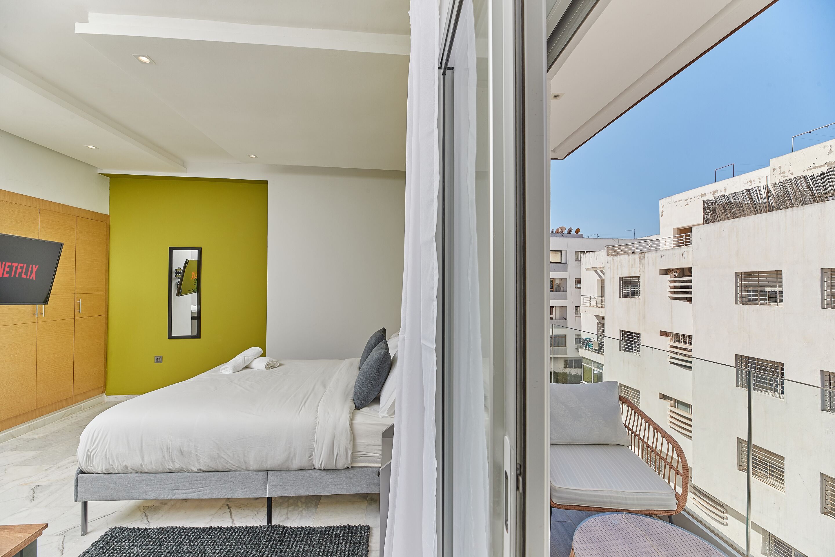Un dormitorio moderno con una cama, una pared de acento verde y vistas de la ciudad desde un balcón.