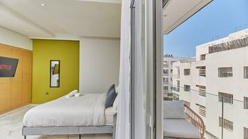 Un dormitorio moderno con una cama, una pared de acento verde y vistas de la ciudad desde un balcón.
