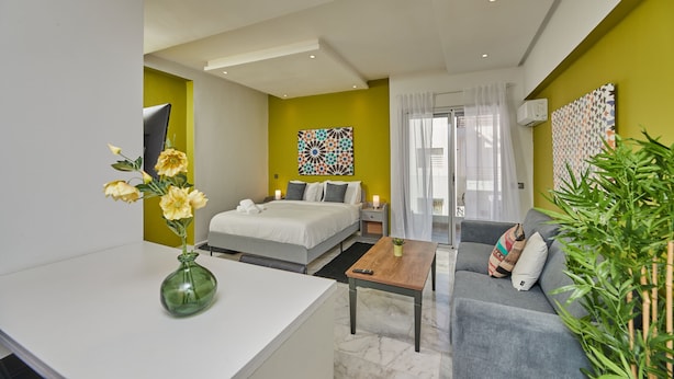 A modern hotel room with a bed, a sofa, a small table, and a green vase with flowers. - StayHere Rabat - Agdal Quiet Living (Rabat)