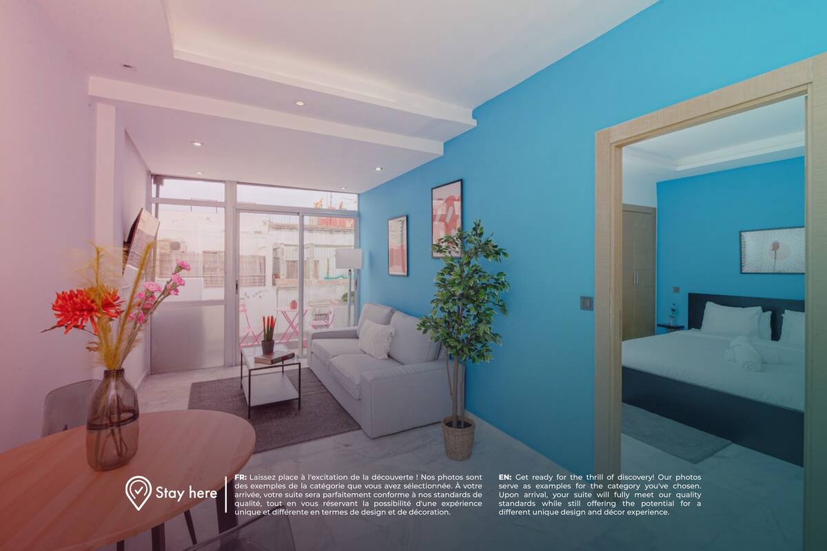 Quarto de hotel moderno com cama grande, sofá, mesa de jantar e planta em vaso.