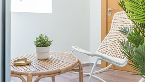 A wicker table with a potted plant and a tray, a white wicker chair, and a wooden door in a room with a tiled floor. - StayHere Rabat - Agdal Quiet Living (Rabat)
