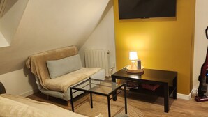 A cozy loft bedroom with a sloped ceiling, a bed, a sofa, a coffee table, and a TV mounted on the wall. - Sous les Toits de Béthune (Béthune)