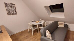 A compact living space with a dining table and chairs, a gray sofa, and a small window. - Sous les Toits de Béthune (Béthune)
