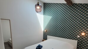 A modern bedroom with a skylight, a bed with rolled towels, a mirror, and patterned wallpaper.