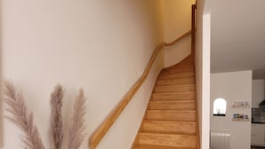 A wooden staircase with a modern design, leading to a kitchen area with white cabinets and a black countertop.