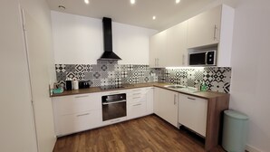 A modern kitchen with white cabinets, a black range hood, patterned backsplash, and a wooden floor.