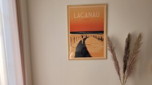 A wooden desk with a vase of pampas grass, a framed picture of a beach scene, and a window with curtains.