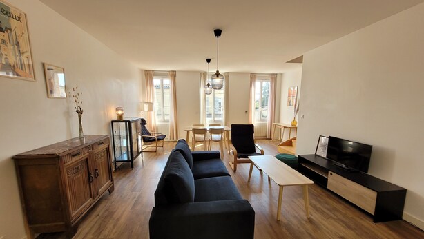 A living room with a black sofa, wooden floor, a TV stand, and a dining area with chairs and a table.