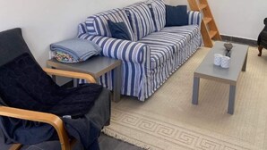 A living room with a striped sofa, a small table, a chair, and a ladder against the wall. - Cosy 1 bed pool house (L'Alfàs del Pi)