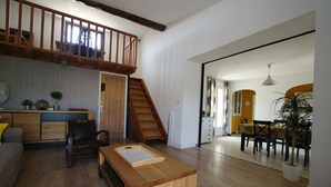 A spacious living area with a wooden coffee table, a sofa, and a dining table with chairs. A staircase leads to an upper level. - 3 bedroom house, private pool, 10min from Pont du Gard (Meynes)