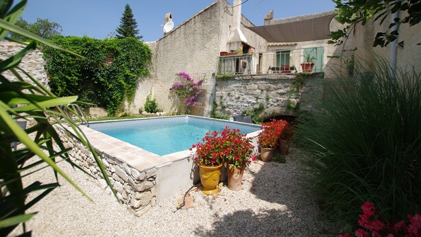 A swimming pool surrounded by a stone wall, potted plants, and a building with a balcony. - 3 bedroom house, private pool, 10min from Pont du Gard (Meynes)