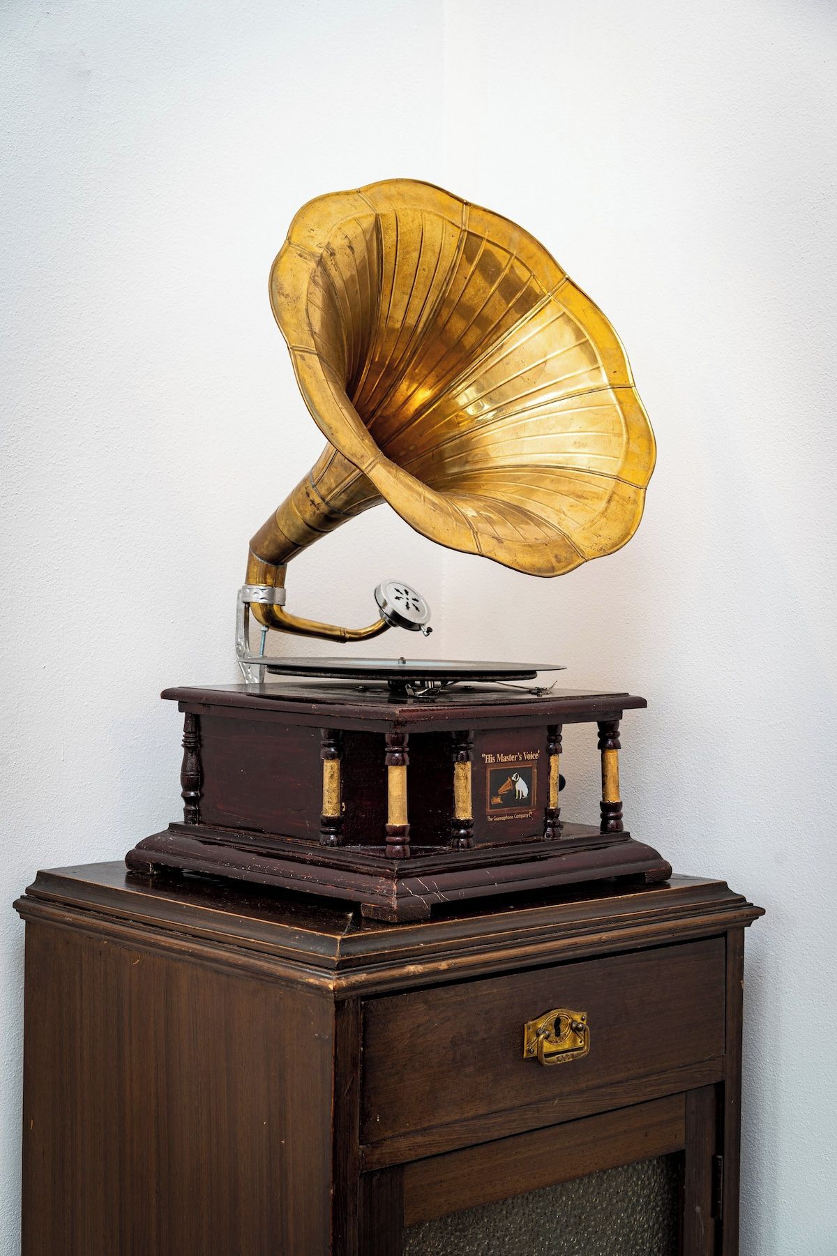 An antique gramophone with a large horn, placed on a wooden cabinet with a drawer.