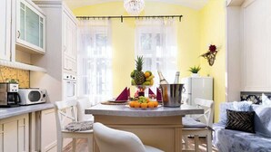 Una cocina compacta con armarios blancos, una zona de comedor con una silla blanca y un sofá azul.
