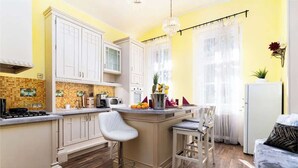 Cocina compacta con armarios blancos, una isla central con taburetes de bar, un refrigerador y un comedor con sofá.