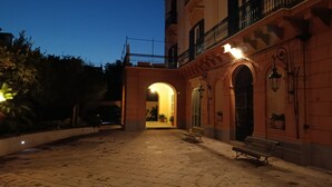 Un patio exterior con un camino empedrado, un banco y la entrada de un edificio con un arco.