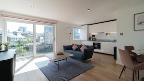 A modern apartment with a living area, kitchen, and large balcony with city views. - PREMIER SUITES Edinburgh Fountain Court (Edinburgh)