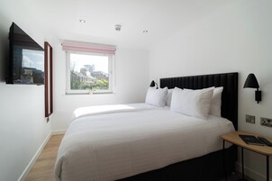 Une chambre à coucher avec un lit, une fenêtre donnant sur un beau paysage, une table de chevet et un téléviseur fixé au mur.