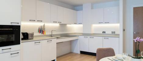 A modern kitchen with white cabinetry, a built-in oven, and a dining area with a round table and chairs.