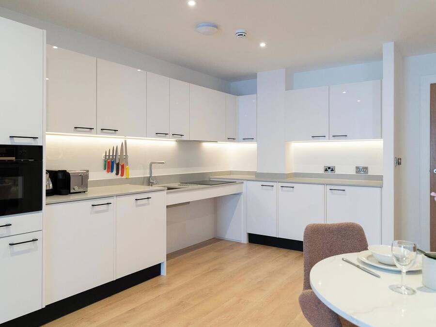 Una cucina moderna con mobili bianchi, forno integrato e zona pranzo con tavolo e sedie rotonde.
