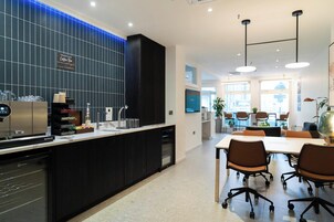 A modern kitchen with a coffee bar, a dining area with a table and chairs, and a view of the city through large windows.