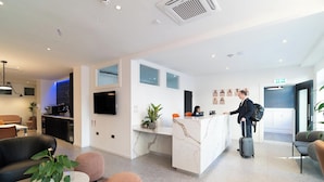A modern hotel lobby with a reception desk, seating area, and a kitchenette. - PREMIER SUITES Edinburgh Fountain Court (Edinburgh)
