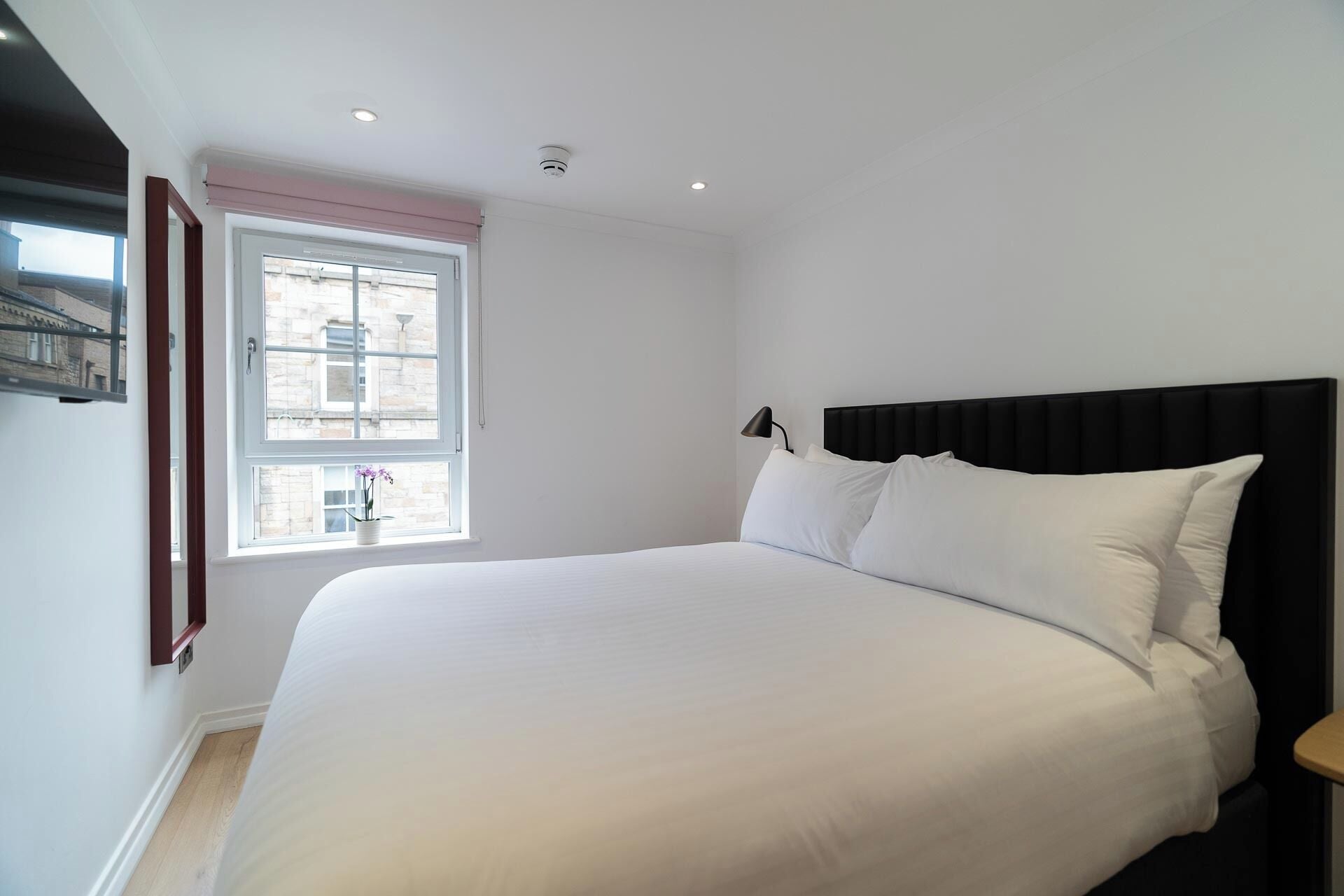 Quarto com cama grande, janela com vista para edifícios e luminária no teto.