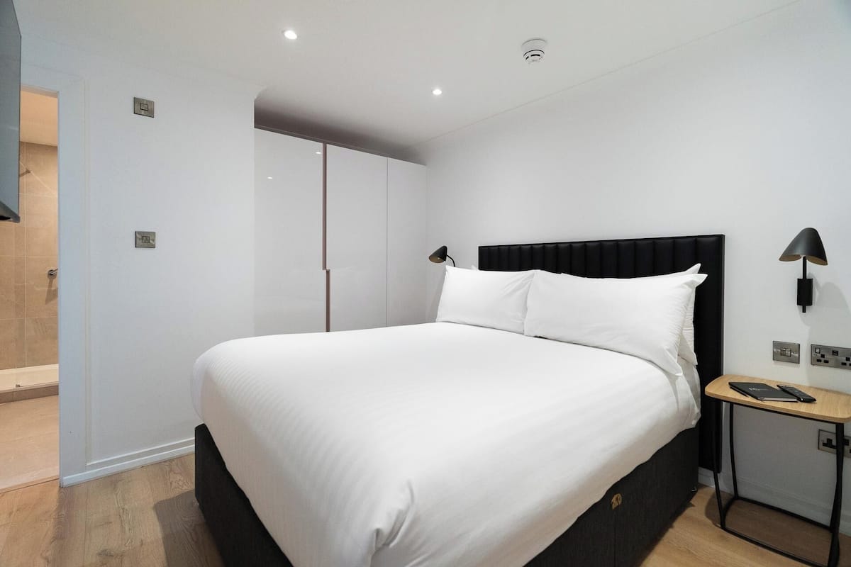 A modern bedroom with a large bed, a nightstand, a desk, and a wardrobe.