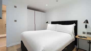A modern bedroom with a large bed, a nightstand, a desk, and a wardrobe.