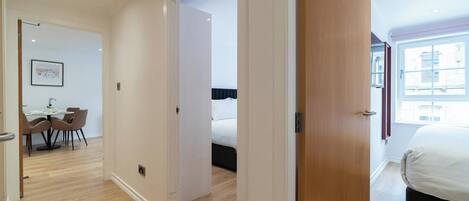 Ein modernes Hotelzimmer mit Holztür, einem Bett, einem Fenster mit Blick auf die Stadt und einem Essbereich mit Tisch und Stühlen.