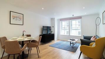 A modern living room with a dining area, a black entertainment unit, and a large window with a view of buildings.
