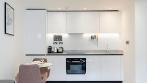 A modern kitchen with white cabinets, a black countertop, and a dining area with a table and chairs. - PREMIER SUITES Edinburgh Fountain Court (Edinburgh)