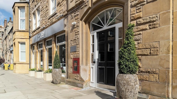 A stone building with a large arched entrance, multiple windows, and potted plants. - PREMIER SUITES Edinburgh Fountain Court (Edinburgh)